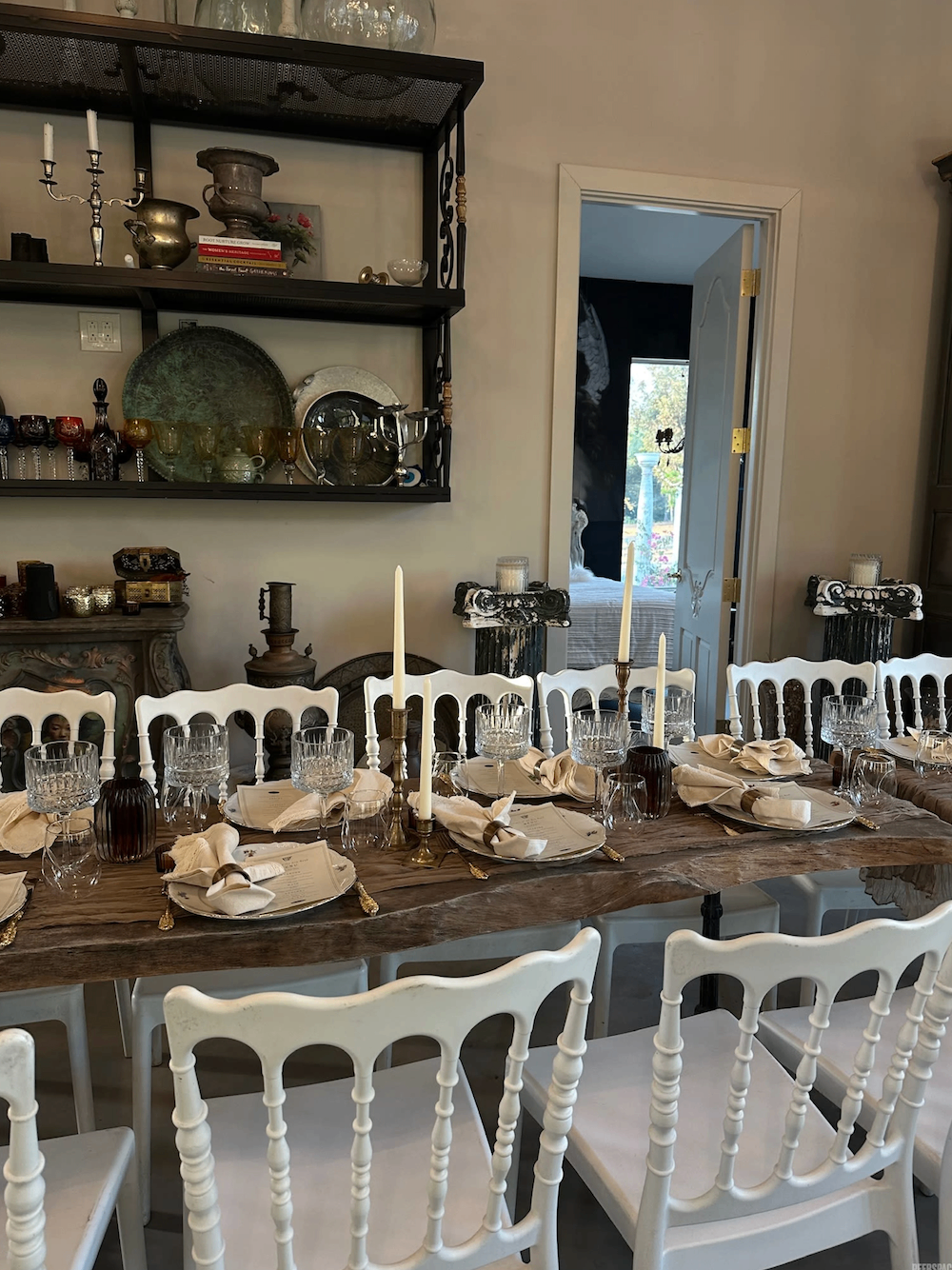Long dining table styled indoors with candles and vintage shelving