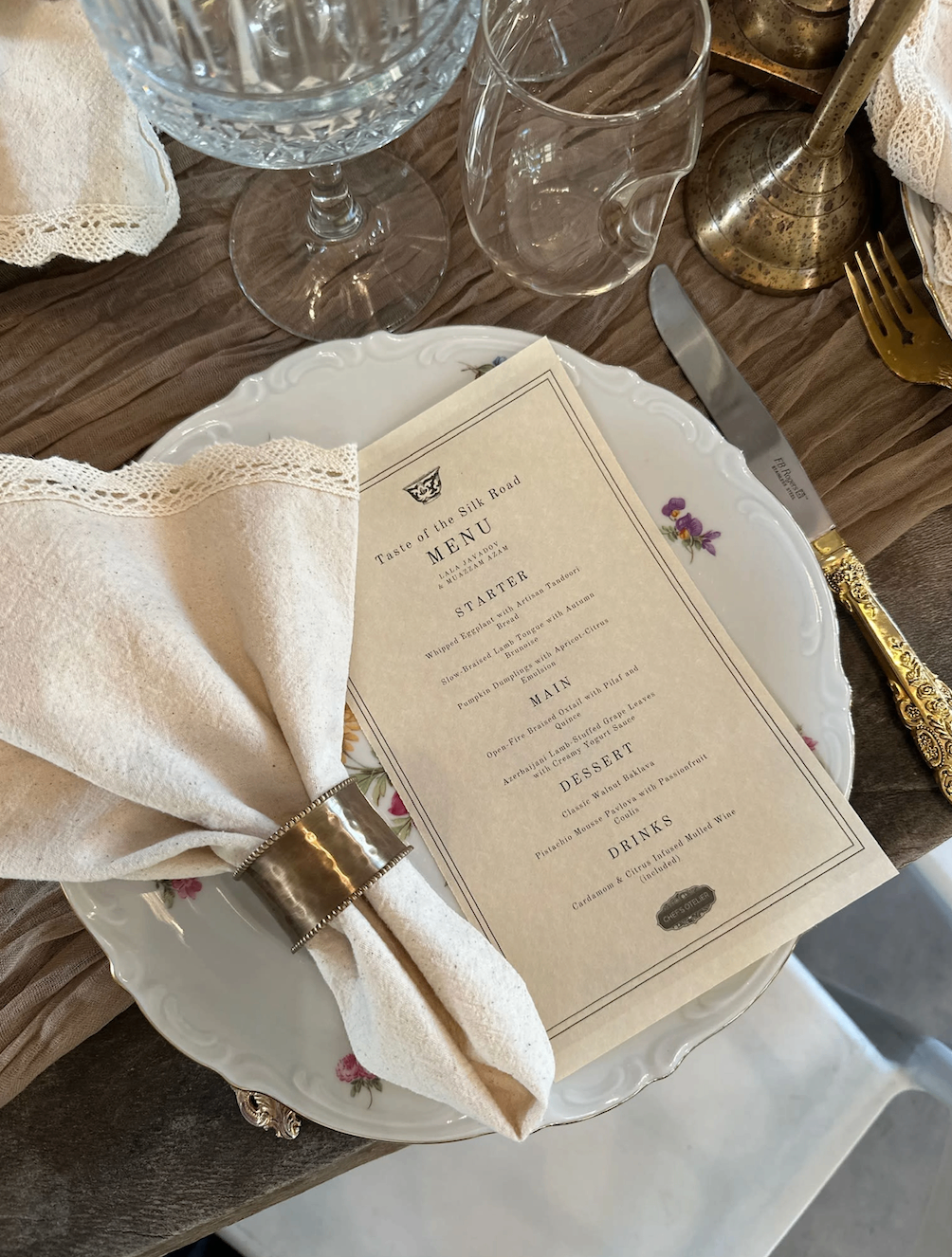Close-up of a place setting with printed menu, vintage plate, and gold flatware
