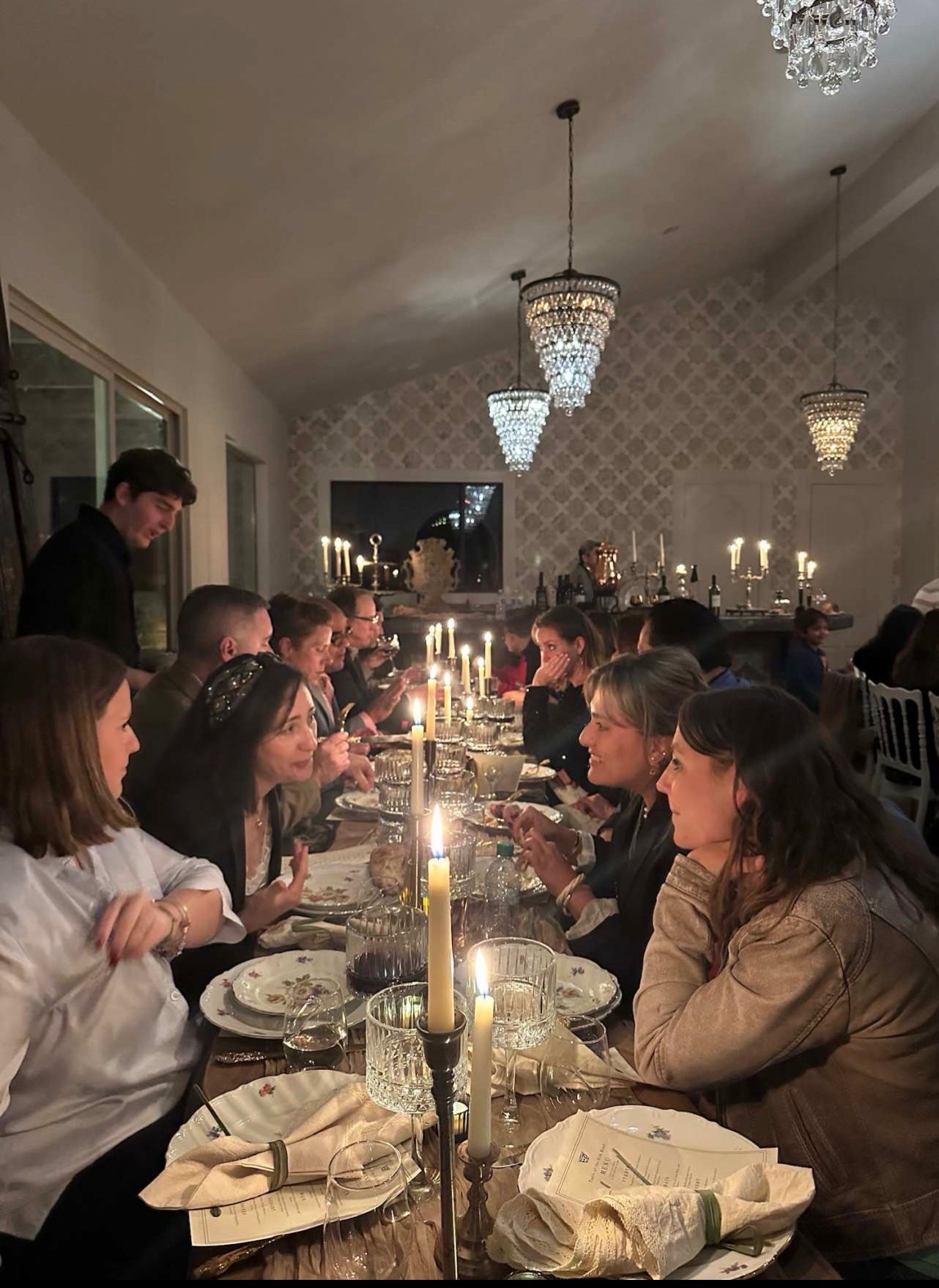 Guests gathered at a long candlelit dinner under chandeliers